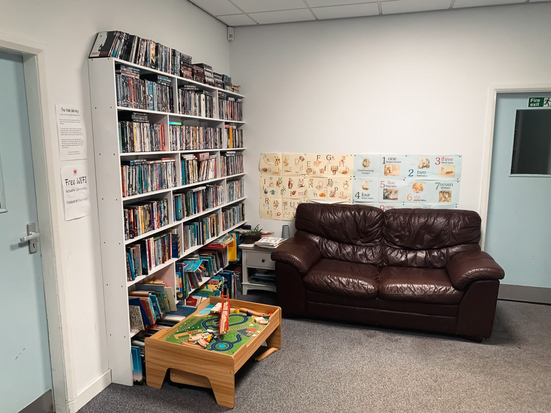 a cosy looking deep brown leather sofa in the library surround by books and childrens toys